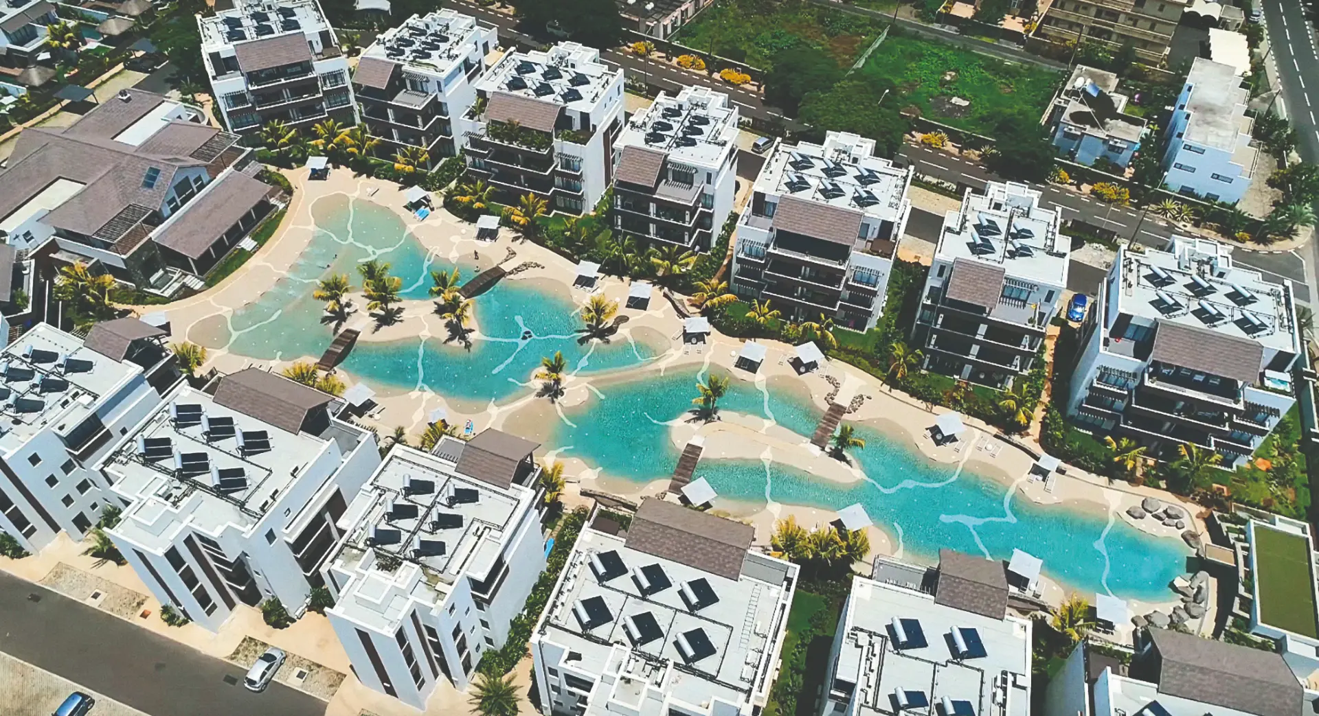 Aerial view of a Bio.design resort installation with multiple sand-sculpted lagoon pools and beach entries