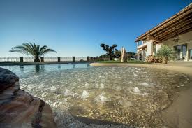 Sand sculpted pool with pebble beach entry beside a villa
