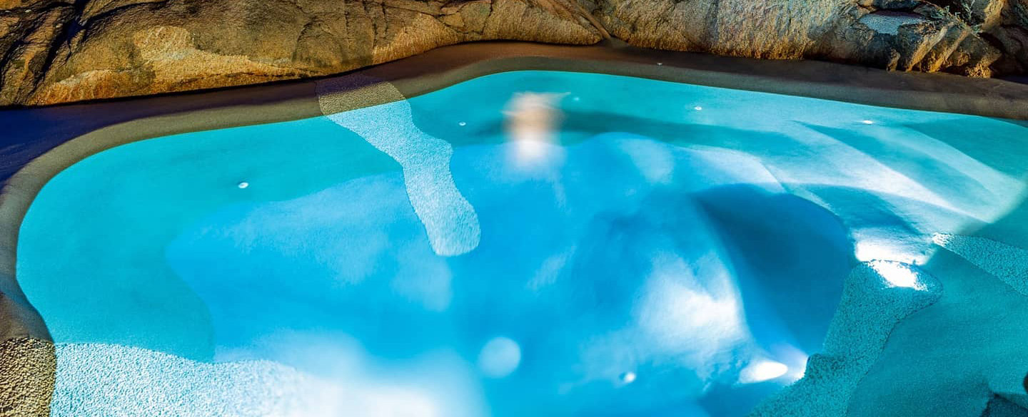 Bio.design pool lit at night with a sculpted beach entry