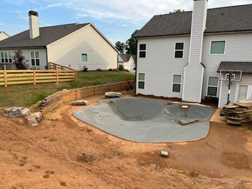 Sculpted pool shell in the ground during construction behind a home