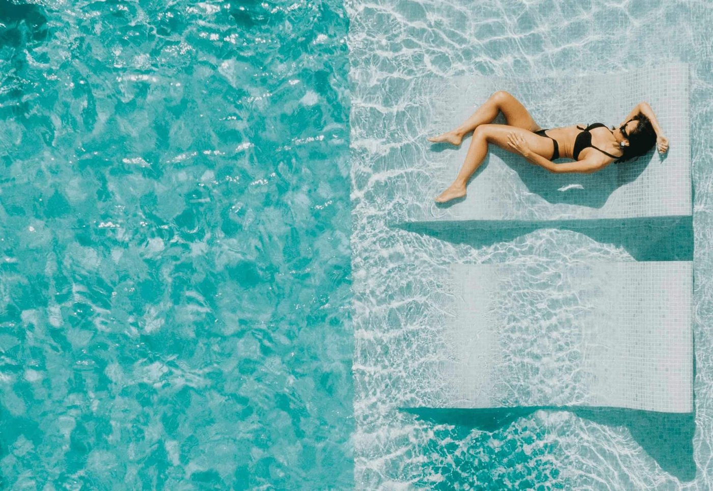 Person relaxing on a pool tanning ledge in a sunny backyard